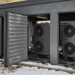 Sechsstufige Wärmepumpenanlage „Energy Unit 2.0“ in der XL-Variante: Außen aufgestellte Luft/Wasser-Wärmepumpenmodule in schallgedämmter Einhausung vor einem Mehrfamilienhaus, teilweise mit geöffneten Schutzgittern.