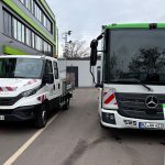 Zwei neue Elektro-Nutzfahrzeuge der Mainzer Entsorgungsbetriebe stehen vor einem modernen Verwaltungsgebäude: links ein weißer Iveco-Transporter mit Ladefläche, rechts ein größerer Mercedes-Benz-Lkw. Vor beiden Fahrzeugen informieren grüne Aufsteller über die Ausstattung und den Einsatz im kommunalen Betrieb.