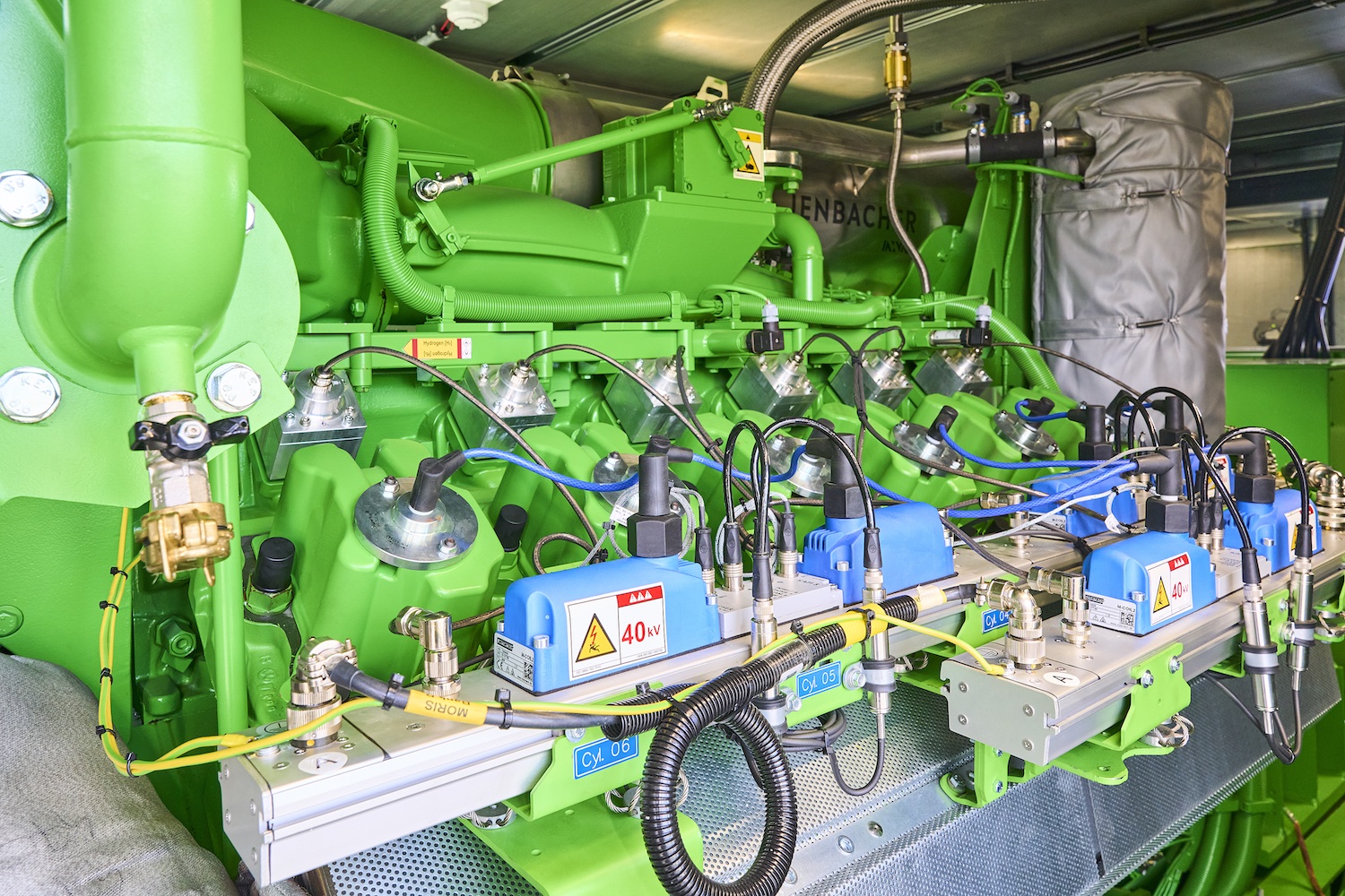 Detailansicht einer Kraft-Wärme-Kopplungsanlage mit grünem Gasmotor, Zylindern, Zündmodulen und Verkabelung in einem Technikraum.