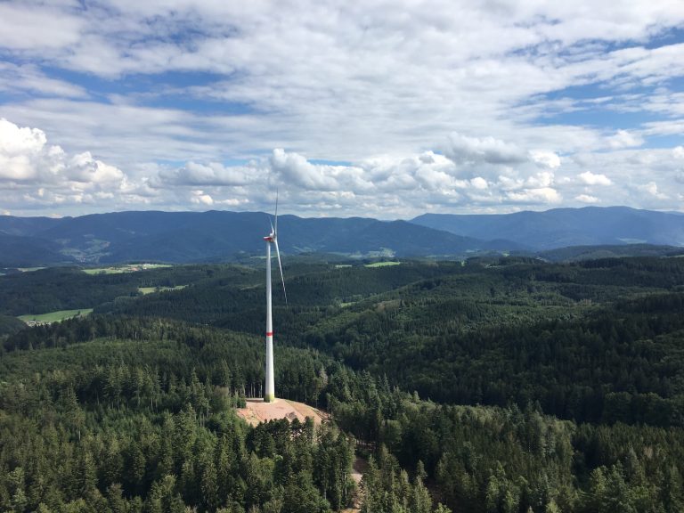 Windenergieanlage auf einer Waldlichtung im Schwarzwald, umgeben von dichtem Wald und Mittelgebirgslandschaft unter wolkigem Himmel.