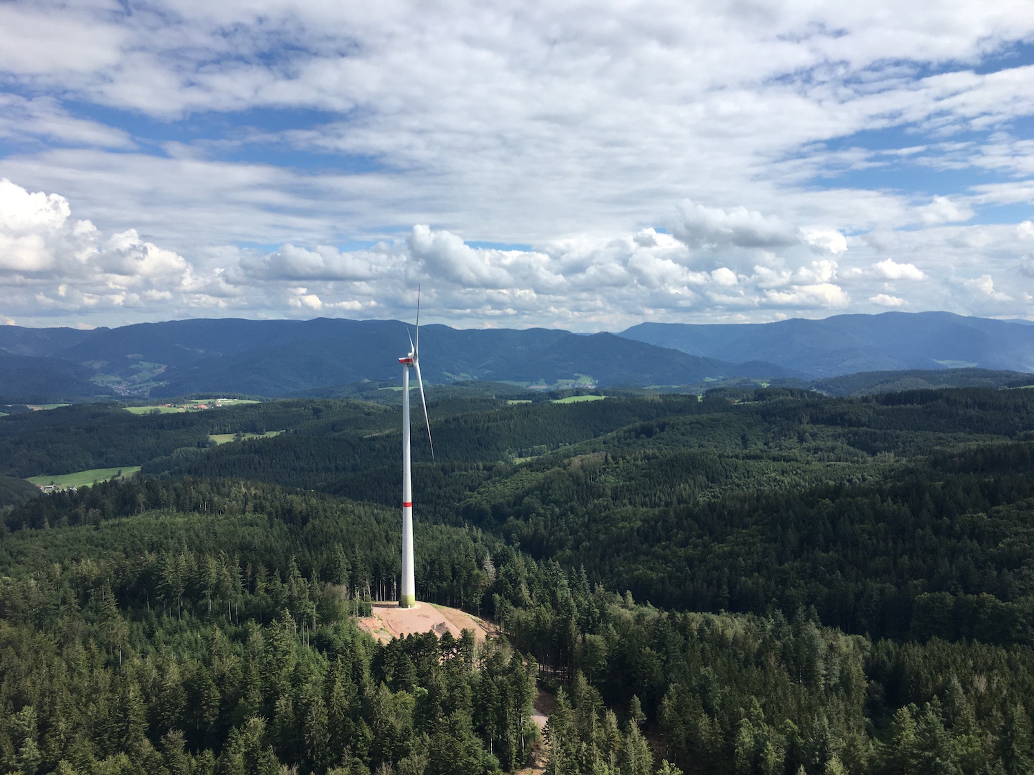 Windenergieanlage auf einer Waldlichtung im Schwarzwald, umgeben von dichtem Wald und Mittelgebirgslandschaft unter wolkigem Himmel.