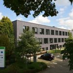 Hauptsitz des Stadtwerks am See in einem modernen, dreigeschossigen Bürogebäude mit grauer Fassade, umgeben von Bäumen und Grünflächen, mit Parkplatz und Firmenschild im Vordergrund.