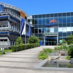 Hauptverwaltung des Energieversorgers Badenova in Freiburg mit moderner Glasfassade, Eingangsbereich und Skulptur vor dem Gebäude.