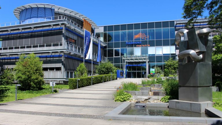 Hauptverwaltung des Energieversorgers Badenova in Freiburg mit moderner Glasfassade, Eingangsbereich und Skulptur vor dem Gebäude.