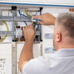 Elektriker installiert und verdrahtet Komponenten in einem geöffneten Zählerschrank mit Kabeln und Klemmenleisten