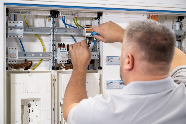 Elektriker installiert und verdrahtet Komponenten in einem geöffneten Zählerschrank mit Kabeln und Klemmenleisten