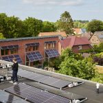 Zwei Personen stehen auf dem Dach eines Mehrfamilienhauses in Hamburg zwischen mehreren Solarmodulen und sprechen miteinander. Im Hintergrund sind weitere Wohnhäuser zu sehen, deren Dächer ebenfalls mit Photovoltaikanlagen ausgestattet sind. Das Bild zeigt ein Mieterstromprojekt mit gemeinschaftlicher Solarstromnutzung in einem Wohnquartier.