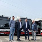 Vier Männer stehen vor drei neuen elektrischen Linienbussen der Stadtwerke Neuss auf einem Betriebshof und präsentieren die moderne, emissionsfreie Fahrzeugflotte.