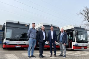 Vier Männer stehen vor drei neuen elektrischen Linienbussen der Stadtwerke Neuss auf einem Betriebshof und präsentieren die moderne, emissionsfreie Fahrzeugflotte.