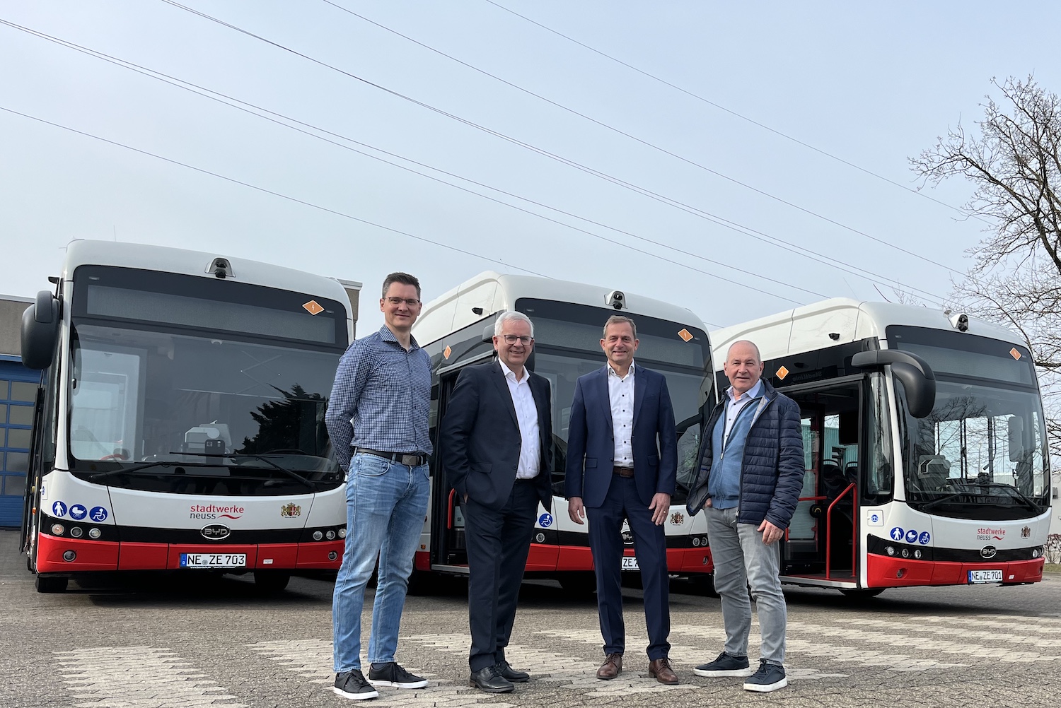 Vier Männer stehen vor drei neuen elektrischen Linienbussen der Stadtwerke Neuss auf einem Betriebshof und präsentieren die moderne, emissionsfreie Fahrzeugflotte.