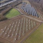 Luftaufnahme des Solarparks Görgeshausen. Im Vordergrund stehen auf einer Ackerfläche mehrere Reihen neuer Metallgestelle für Solarmodule, teils noch ohne Paneele. Im oberen Bildbereich sind bereits fertig montierte Solarmodulreihen zu sehen. Links verlaufen eine Autobahn und eine Bahnstrecke parallel am Gelände vorbei. Rechts grenzt ein bewaldeter Hang an den Solarpark. Rundherum liegen Felder, Wiesen und am oberen linken Rand Wohnhäuser des Ortes.