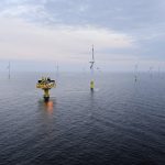 Offshore-Windpark Baltic 1 in der Ostsee: Mehrere Windkraftanlagen stehen in gleichmäßigen Abständen im offenen Meer. Im Vordergrund ist eine Plattform für Technik oder Wartung zu sehen, dahinter drehen sich die Rotoren der Windräder unter einem bewölkten Himmel.