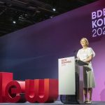 Kerstin Andreae, Vorsitzende der Hauptgeschäftsführung des Bundesverbands der Energie- und Wasserwirtschaft (BDEW), spricht auf der Bühne des BDEW-Kongresses 2026 an einem Rednerpult. Hinter ihr ist das Kongresslogo auf einer großflächigen, violett beleuchteten Bühnenwand zu sehen. Im Vordergrund stehen die roten Buchstaben des BDEW-Logos. Die Aufnahme zeigt ihren Auftritt während der Eröffnung der Fachveranstaltung.
