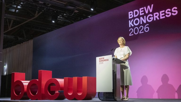 Kerstin Andreae, Vorsitzende der Hauptgeschäftsführung des Bundesverbands der Energie- und Wasserwirtschaft (BDEW), spricht auf der Bühne des BDEW-Kongresses 2026 an einem Rednerpult. Hinter ihr ist das Kongresslogo auf einer großflächigen, violett beleuchteten Bühnenwand zu sehen. Im Vordergrund stehen die roten Buchstaben des BDEW-Logos. Die Aufnahme zeigt ihren Auftritt während der Eröffnung der Fachveranstaltung.