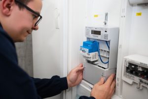 Ein Techniker installiert ein intelligentes Messsystem (Smart Meter) in einem Stromzählerkasten. Das digitale Messgerät mit Kommunikationsmodul wird in die bestehende Strominfrastruktur eingebaut und ermöglicht die automatische Erfassung und Übermittlung von Verbrauchsdaten.