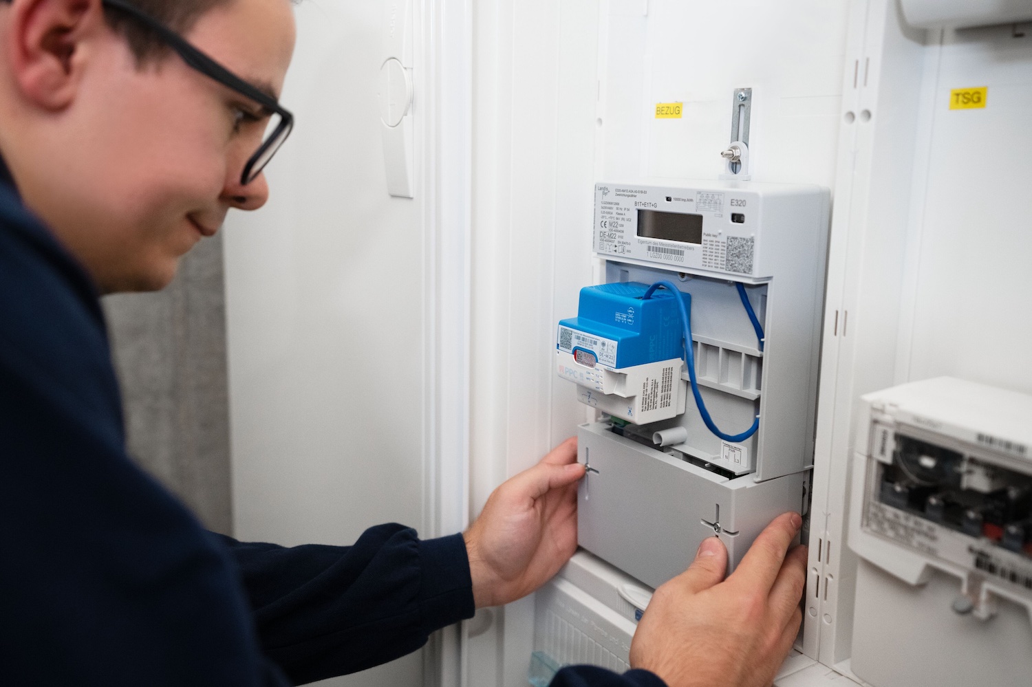 Ein Techniker installiert ein intelligentes Messsystem (Smart Meter) in einem Stromzählerkasten. Das digitale Messgerät mit Kommunikationsmodul wird in die bestehende Strominfrastruktur eingebaut und ermöglicht die automatische Erfassung und Übermittlung von Verbrauchsdaten.