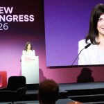 Bundeswirtschaftsministerin Katharina Reiche spricht auf dem BDEW-Kongress 2026 an einem Rednerpult vor einem großen Publikum. Hinter ihr zeigt eine überdimensionale Leinwand eine Nahaufnahme der Ministerin während ihrer Rede. Der Bühnenhintergrund ist in violetten und magentafarbenen Tönen gestaltet und trägt das Logo „BDEW Kongress 2026“.
