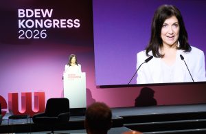 Bundeswirtschaftsministerin Katharina Reiche spricht auf dem BDEW-Kongress 2026 an einem Rednerpult vor einem großen Publikum. Hinter ihr zeigt eine überdimensionale Leinwand eine Nahaufnahme der Ministerin während ihrer Rede. Der Bühnenhintergrund ist in violetten und magentafarbenen Tönen gestaltet und trägt das Logo „BDEW Kongress 2026“.