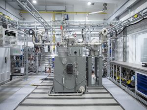 Blick in eine helle Versuchshalle mit einem technisch komplexen Einzylinder-Teststand. Im Zentrum steht eine großformatige Forschungsanlage aus Metall mit zahlreichen Rohrleitungen, Ventilen, Messinstrumenten und Steuerungseinheiten. Die Anlage ist von weiterer Labor- und Prüftechnik umgeben und dient der Untersuchung motorischer Verbrennungsprozesse von Wasserstoff und Ammoniak am WTZ Roßlau.