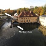 Luftaufnahme des historischen Isarwerks 1 an der Isar. Pfeile markieren den alten Leerschuss vor dem Kraftwerk sowie den Standort des geplanten neuen Technikgebäudes.
