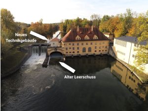 Luftaufnahme des historischen Isarwerks 1 an der Isar. Pfeile markieren den alten Leerschuss vor dem Kraftwerk sowie den Standort des geplanten neuen Technikgebäudes.