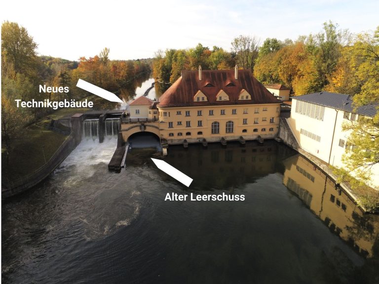 Luftaufnahme des historischen Isarwerks 1 an der Isar. Pfeile markieren den alten Leerschuss vor dem Kraftwerk sowie den Standort des geplanten neuen Technikgebäudes.
