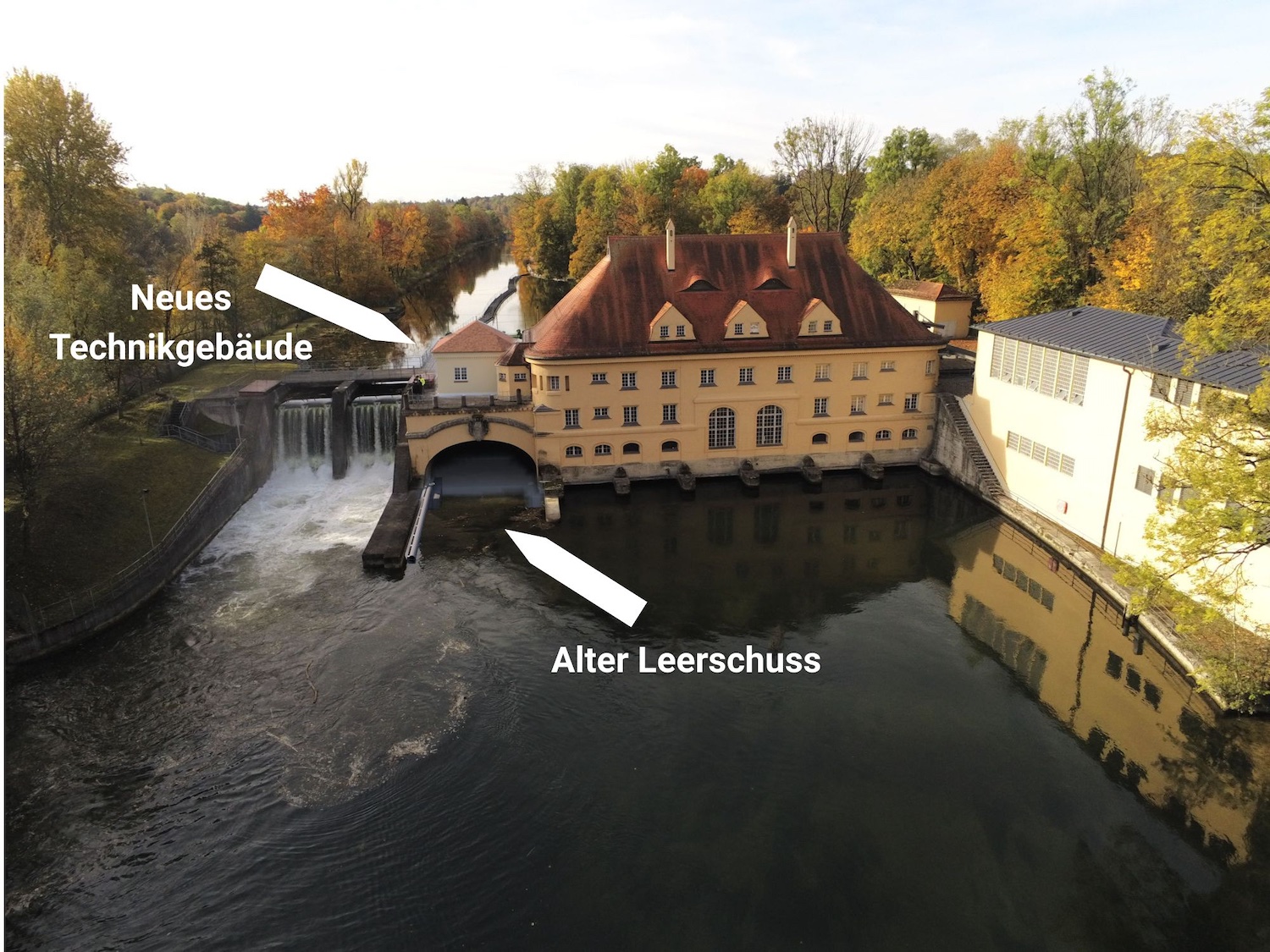 Luftaufnahme des historischen Isarwerks 1 an der Isar. Pfeile markieren den alten Leerschuss vor dem Kraftwerk sowie den Standort des geplanten neuen Technikgebäudes.